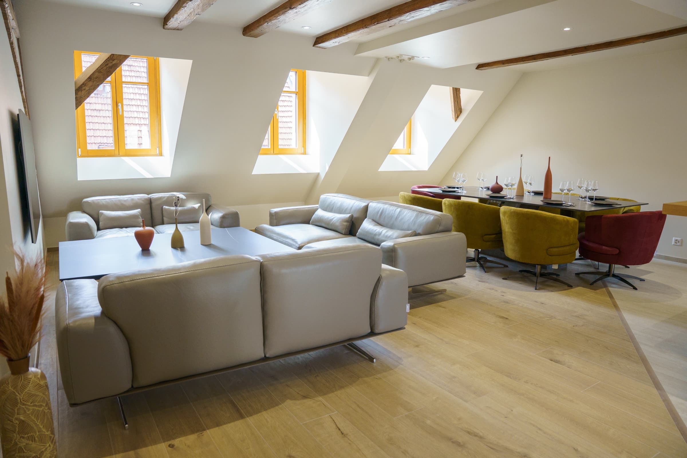 Séjour 65 m² du Rooftop avec canapés cuir gris et table à manger sous poutres apparentes
